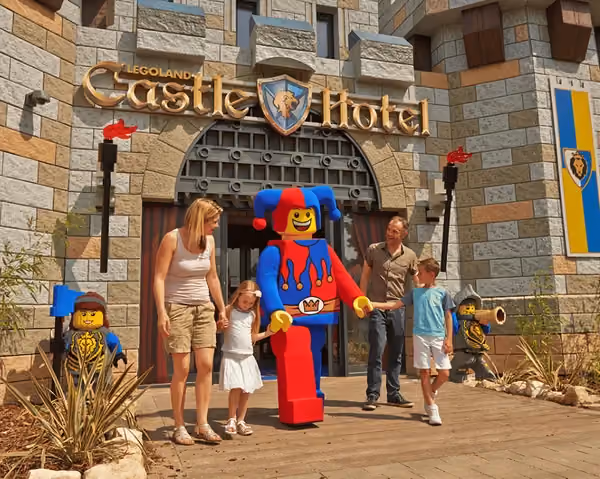 Photo of the exterior of the LEGO castle hotel with a LEGO figure in the middle walking in a line with two children, mother and father
