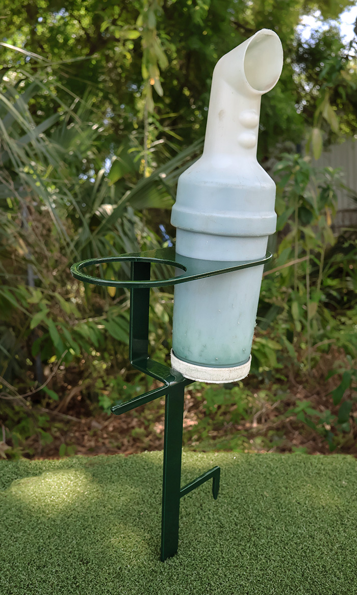 White plastic divot mix bottle holder resting in a green steel stake inserted into artificial grass with greenery background.
