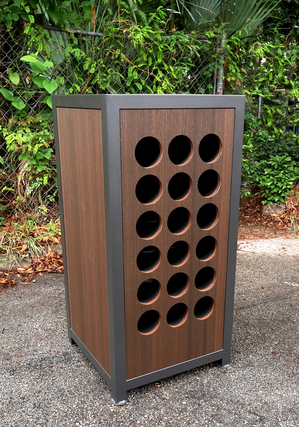 Tall wooden bottle holder with 15 round holes in a 3 by 5 grid, outdoors on pavement.