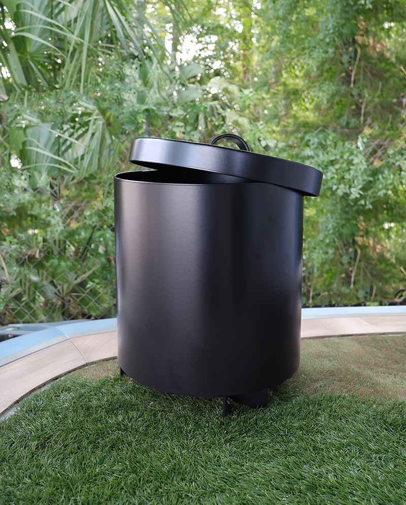 Black cylindrical divot mix can with slightly open lid on green grass with plants background.