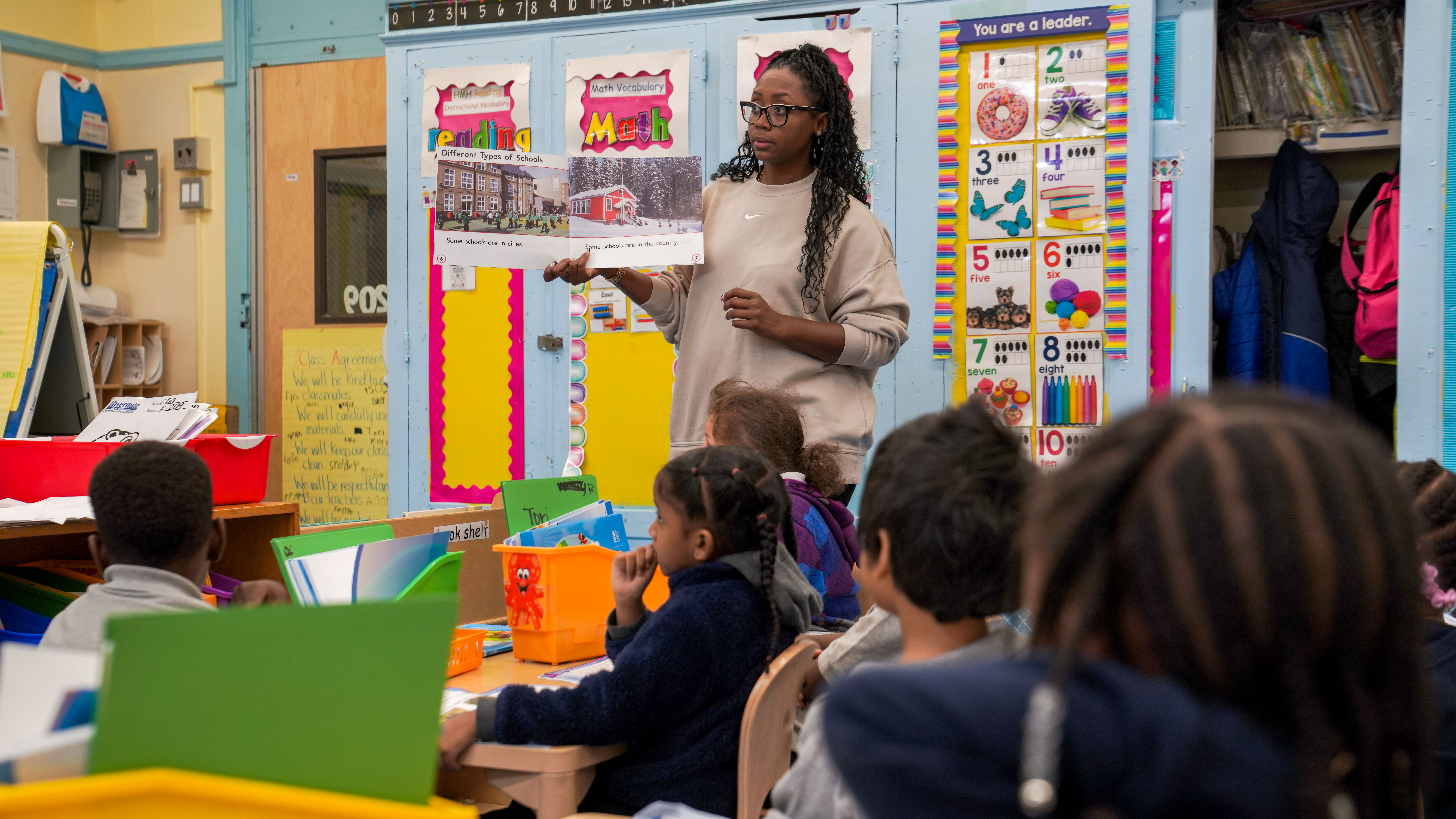 Teacher holding up a book about different types of schools to students
