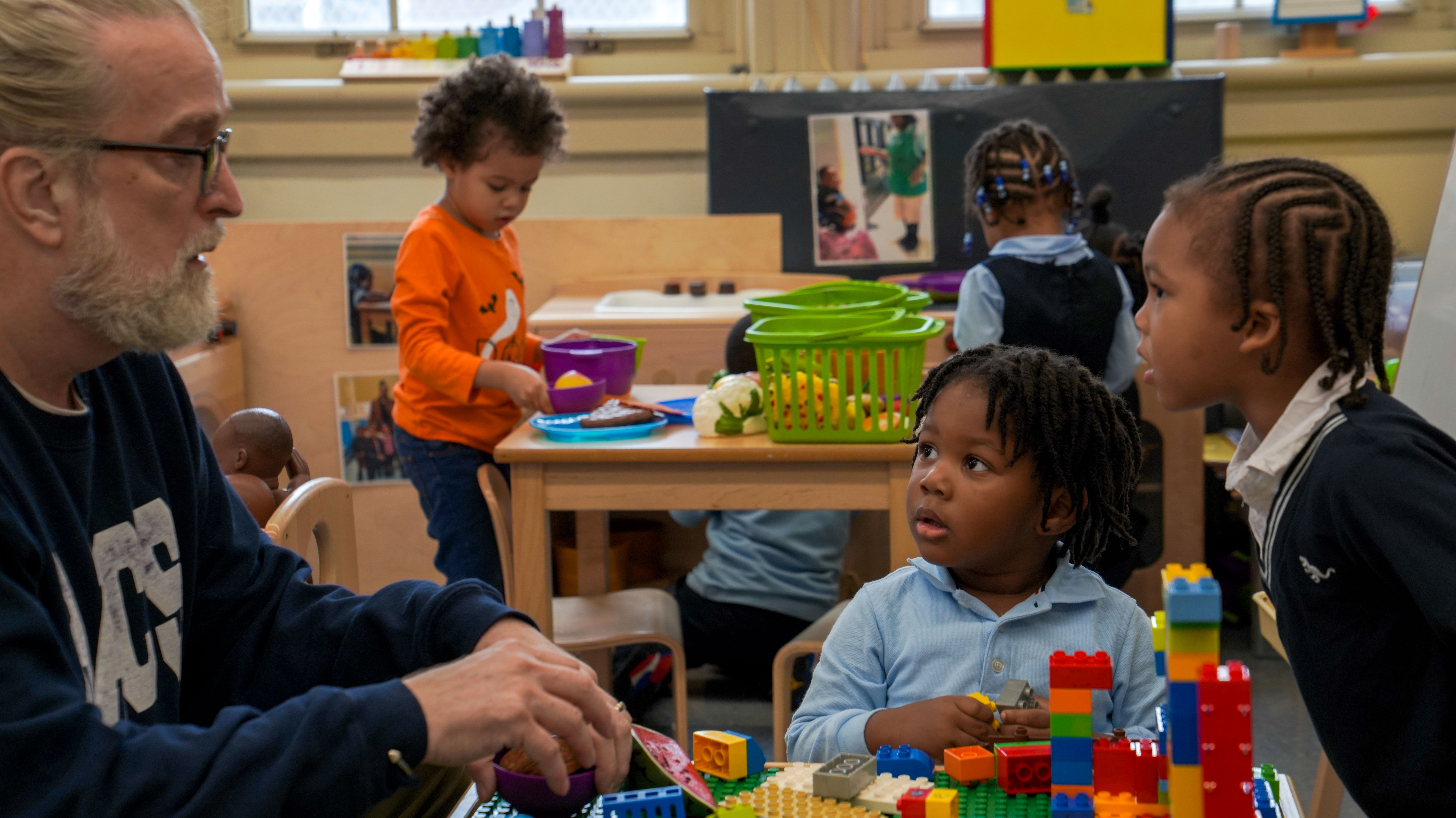 Teacher and young students building with colorful blocks in classroom