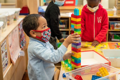 Young student building a tall colorful block tower in classroom