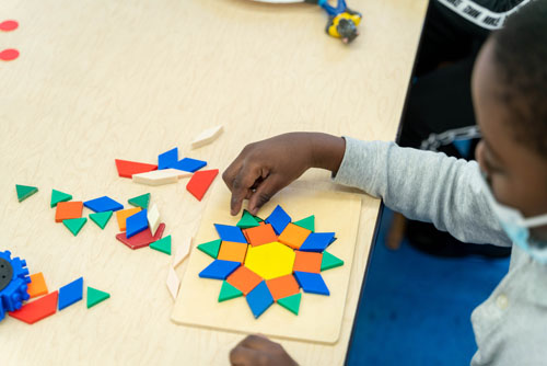 Student arranging colorful geometric pattern blocks on a board