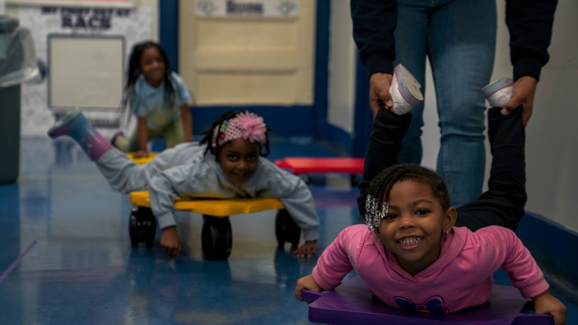 Students riding scooter boards during physical education class indoors