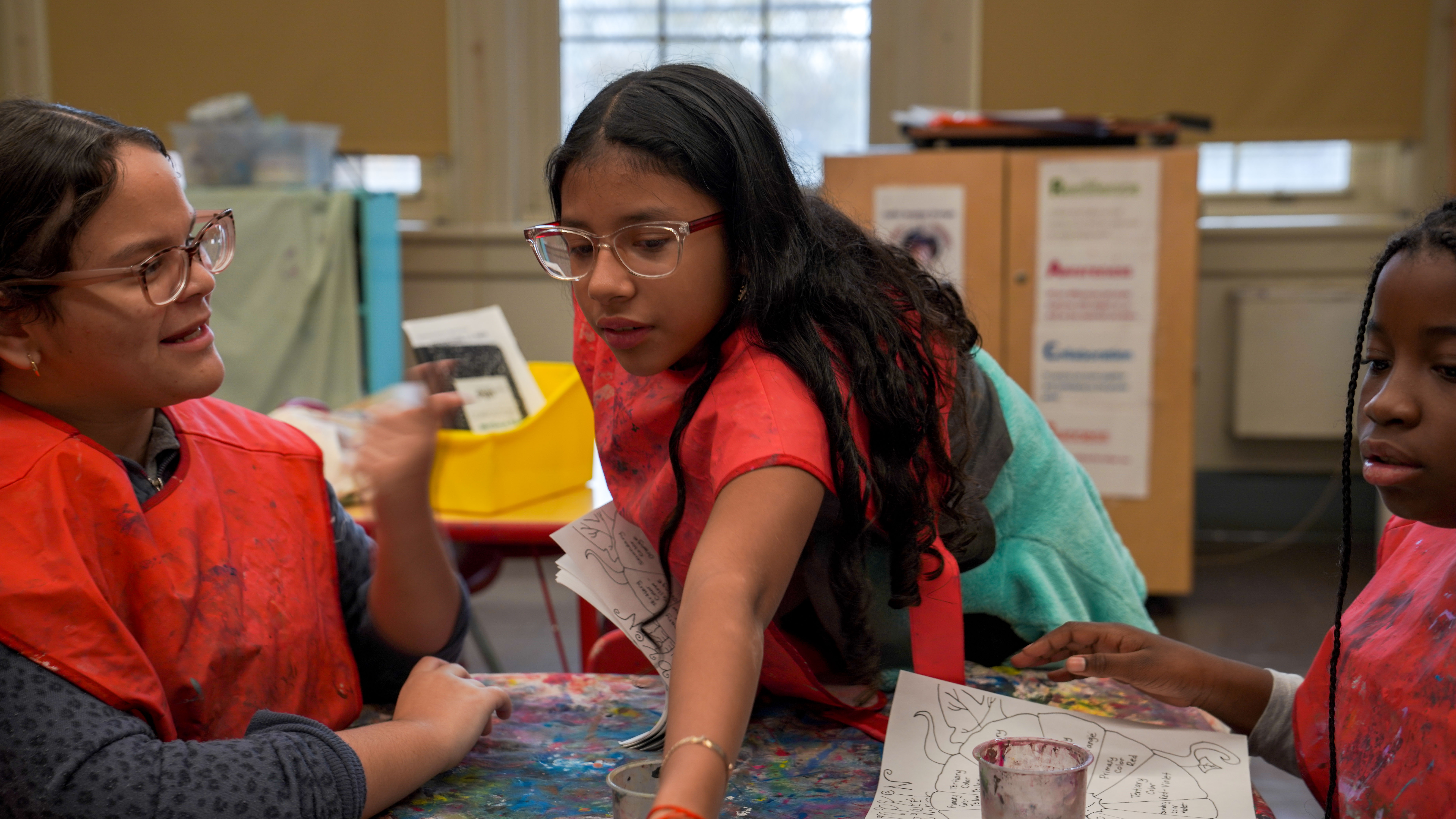 Three students in paint smocks collaborate on an art project