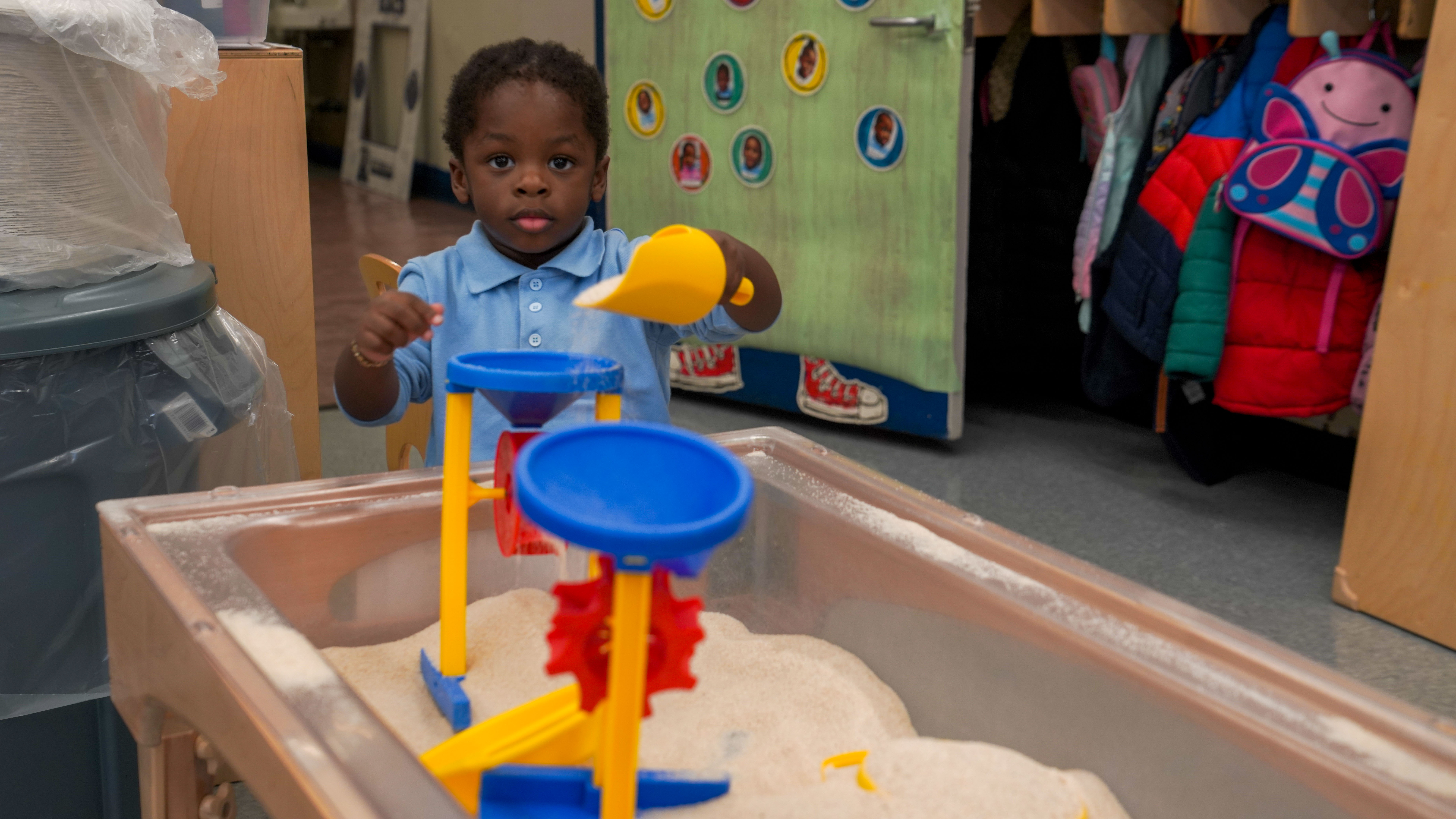 Young student exploring a sand and water sensory table in classroom