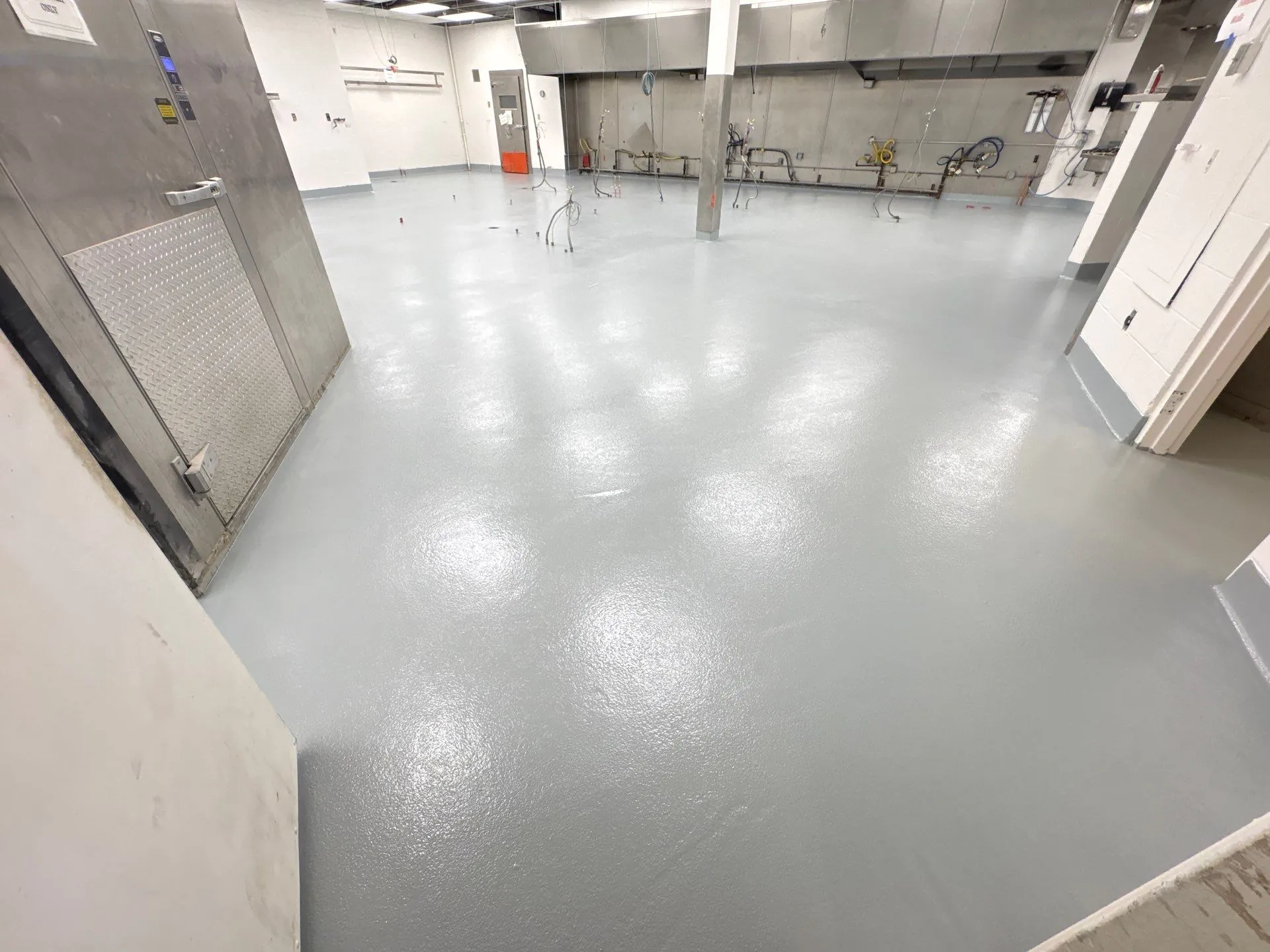Empty industrial room with smooth, light gray self-leveling epoxy floor and exposed pipes.