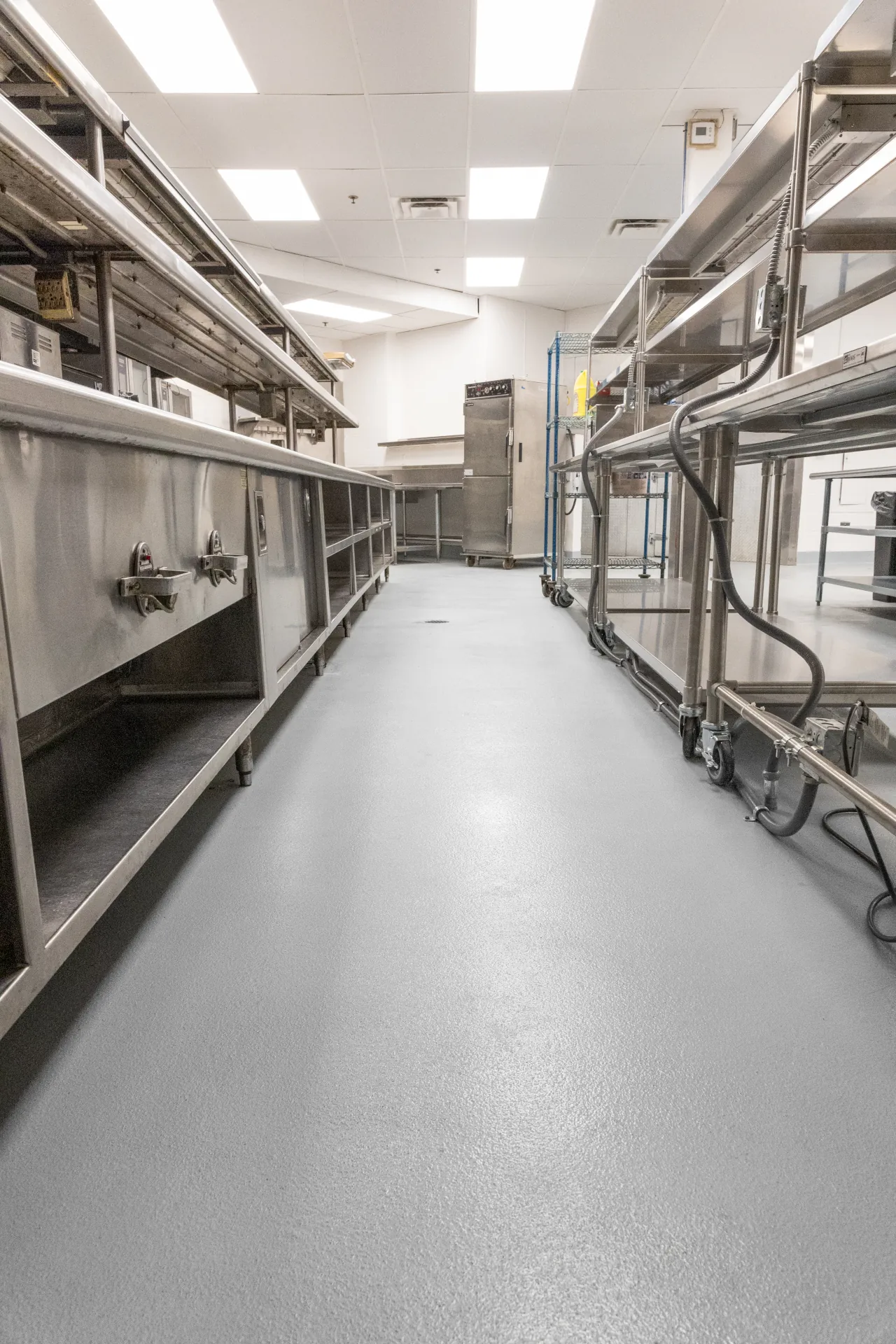 Empty commercial kitchen with clean cementitious urethane floor and stainless steel counters and shelves.