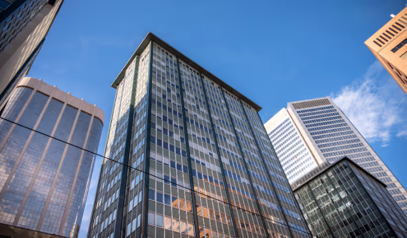 View looking up at several modern tall glass and steel office buildings under a blue sky with a few clouds.