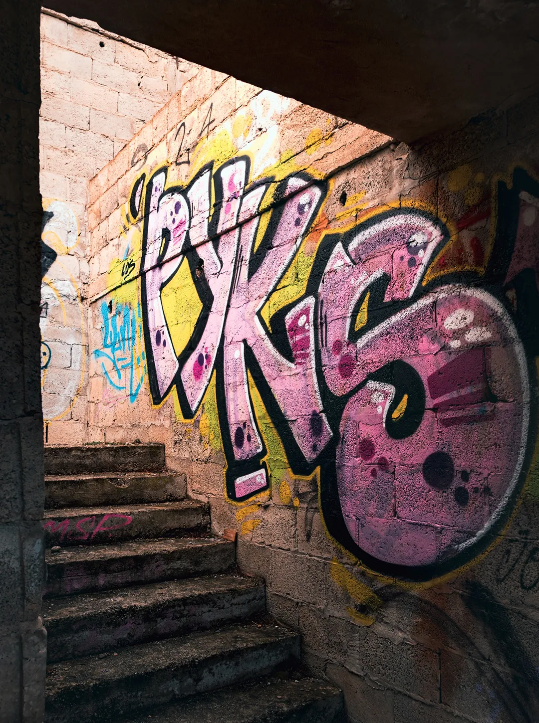 Stone staircase ascending with graffiti art on the wall featuring large pink letters PKS outlined in black and yellow.