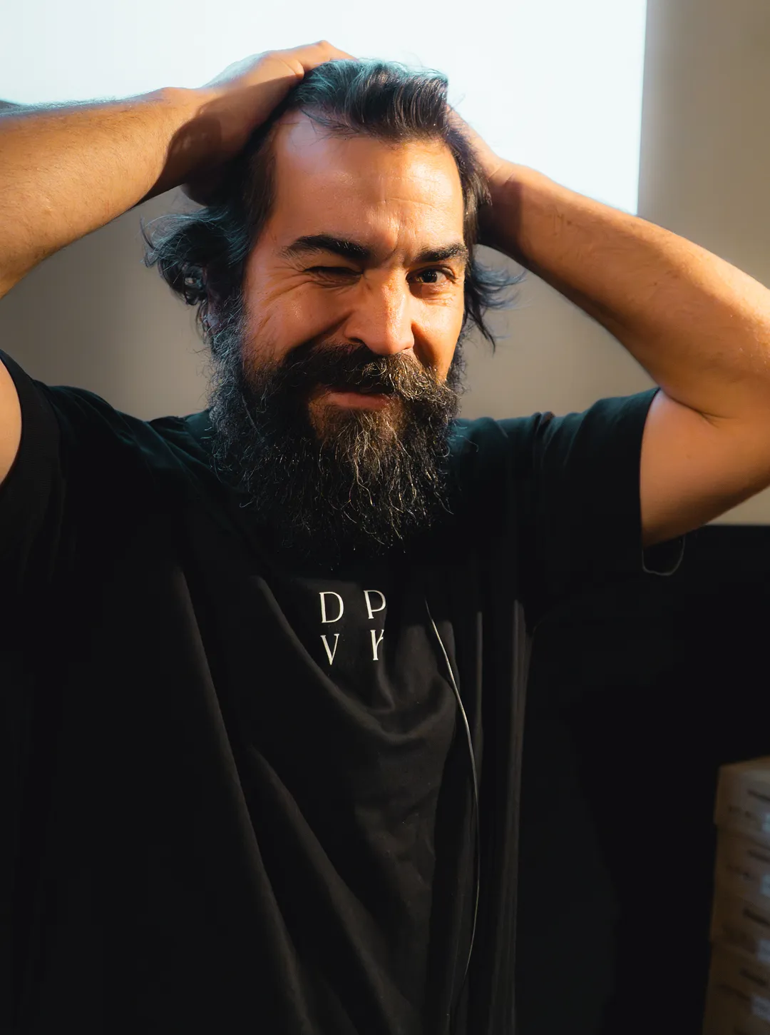 Bearded man Marcio Lopes with dark hair smiling and winking while holding his head with both hands.