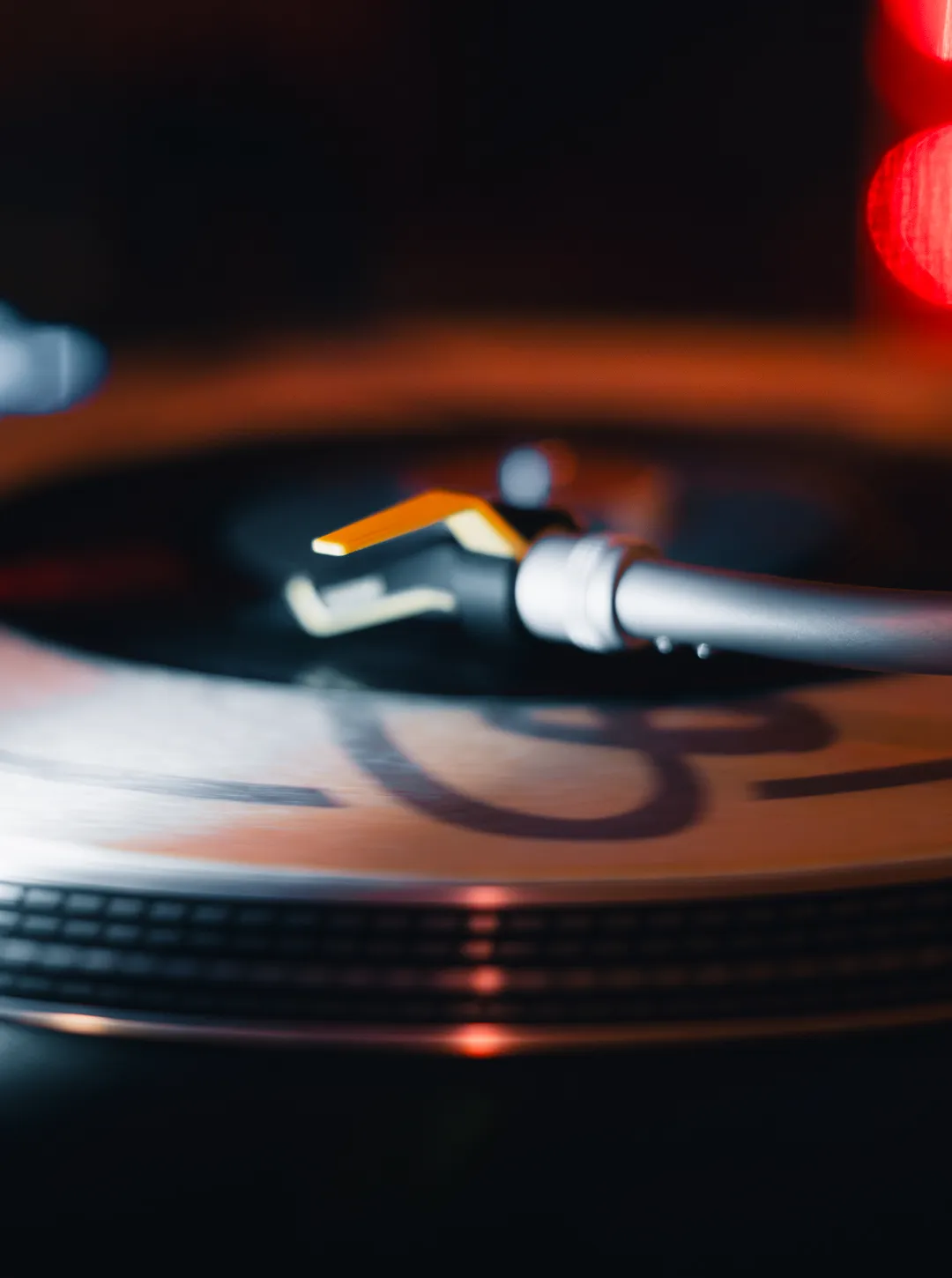 Two men in a music studio, one adjusting controls on equipment and the other watching, with a turntable in the foreground and synthesizers on the wall behind.