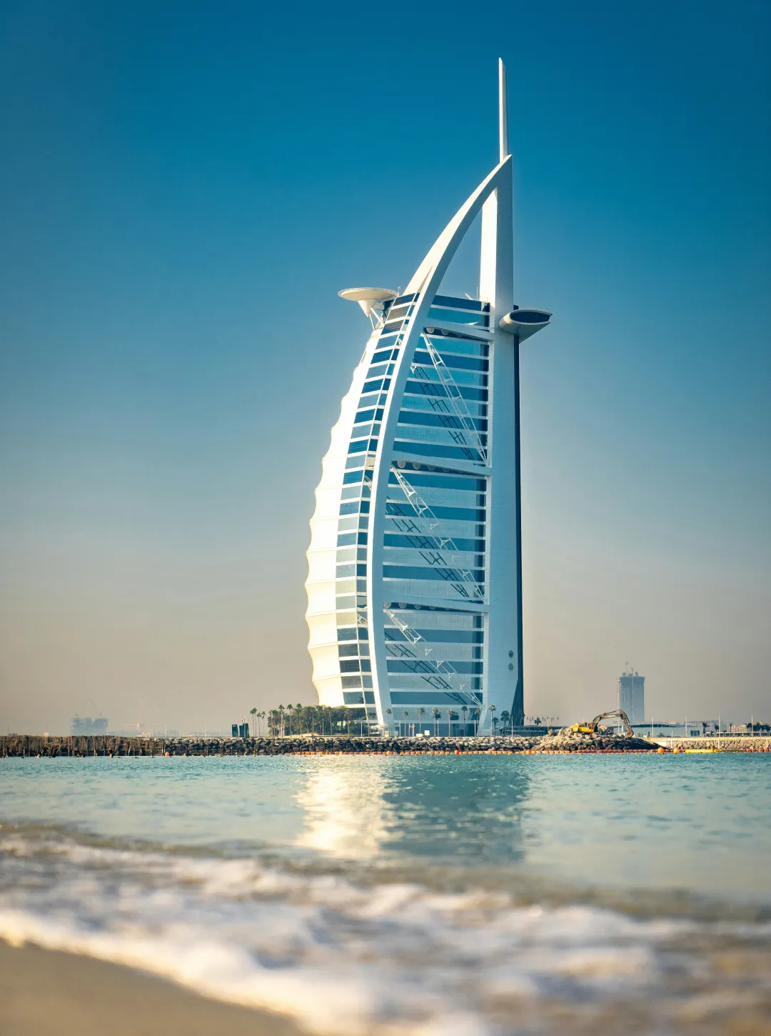 Burj Al Arab hotel standing on an artificial island with calm sea and clear blue sky background.
