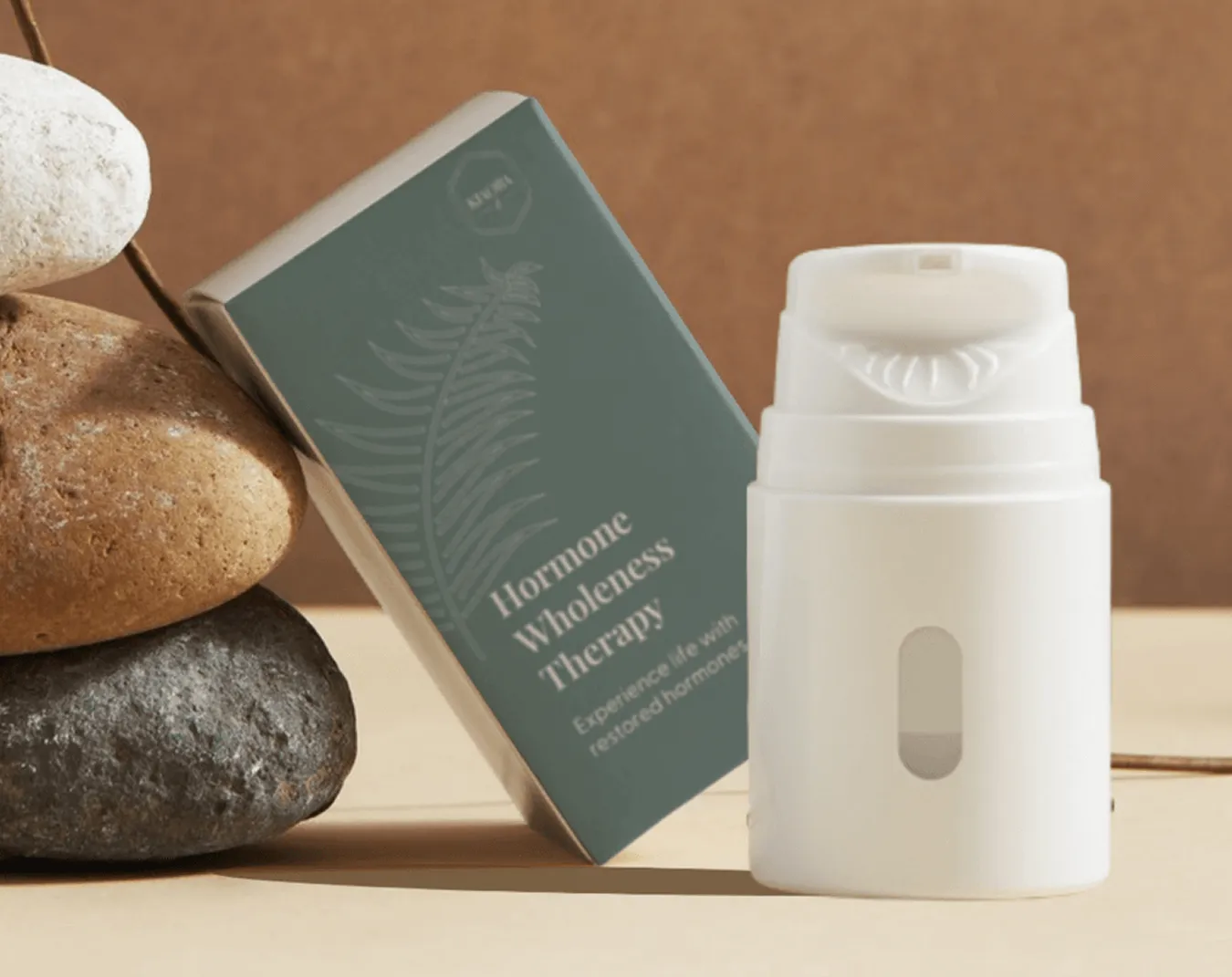 White hormone therapy dispenser bottle next to its green box labeled 'Hormone Wholeness Therapy' and a stack of smooth stones.
