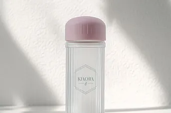 Clear cylindrical bottle with a pink cap and KIAORA logo on a light textured background.