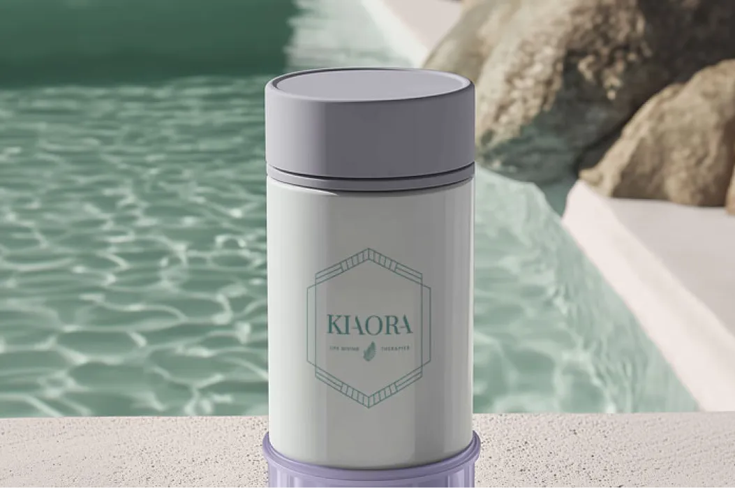 Kaora branded water bottle with a grey lid placed on a textured surface by a pool with clear water and rocks nearby.