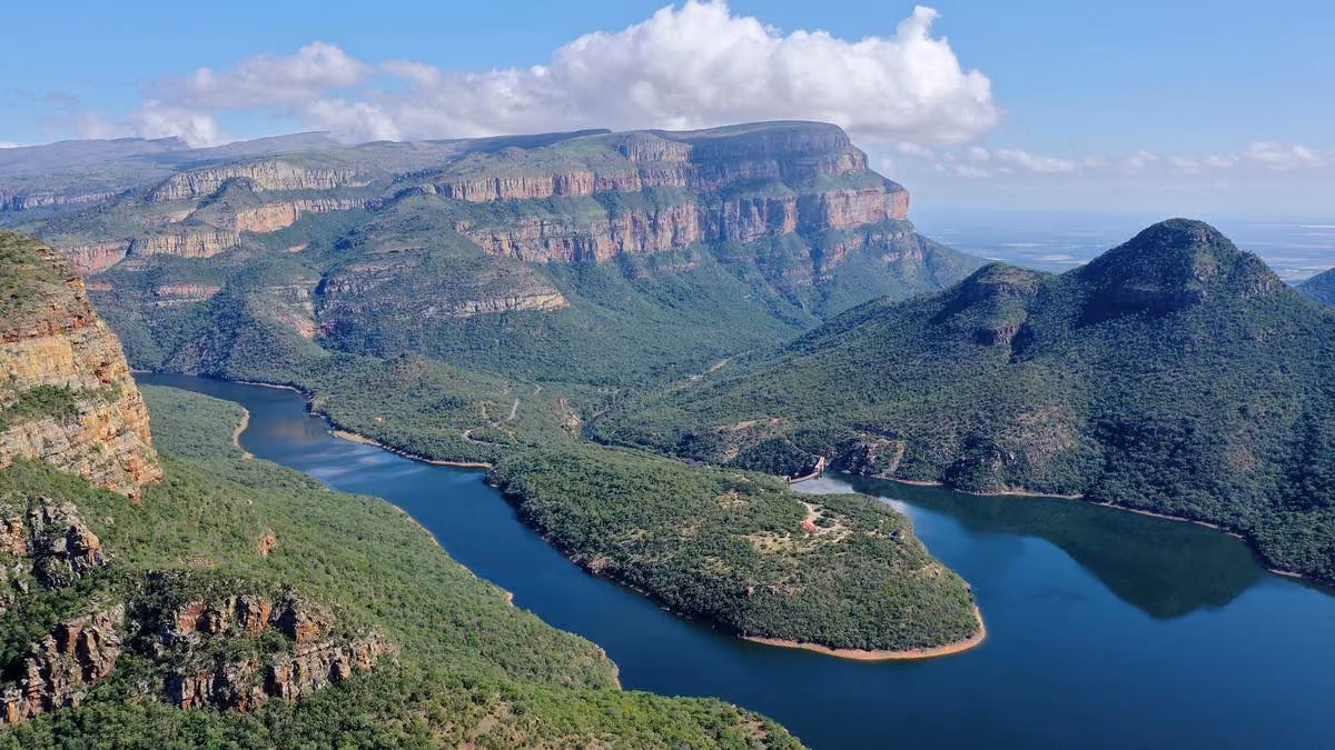A breathtaking panoramic view of the lush, green Blyde River Canyon, featuring a winding blue river below and towering, flat-topped mountain peaks in the distance