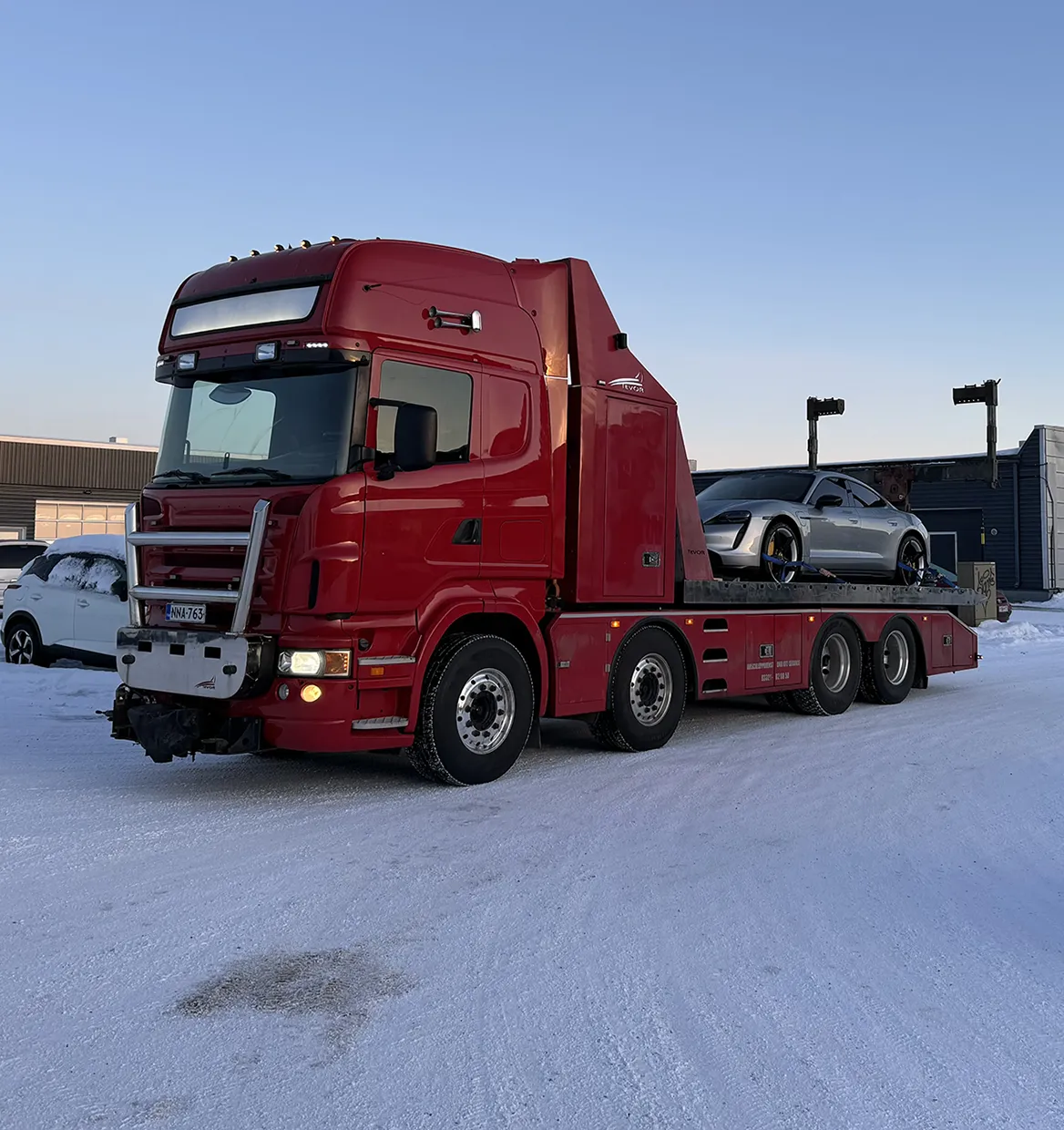 Punainen hinaus auto siirtämässä sähköautoa lumisella tiellä yritys alueella