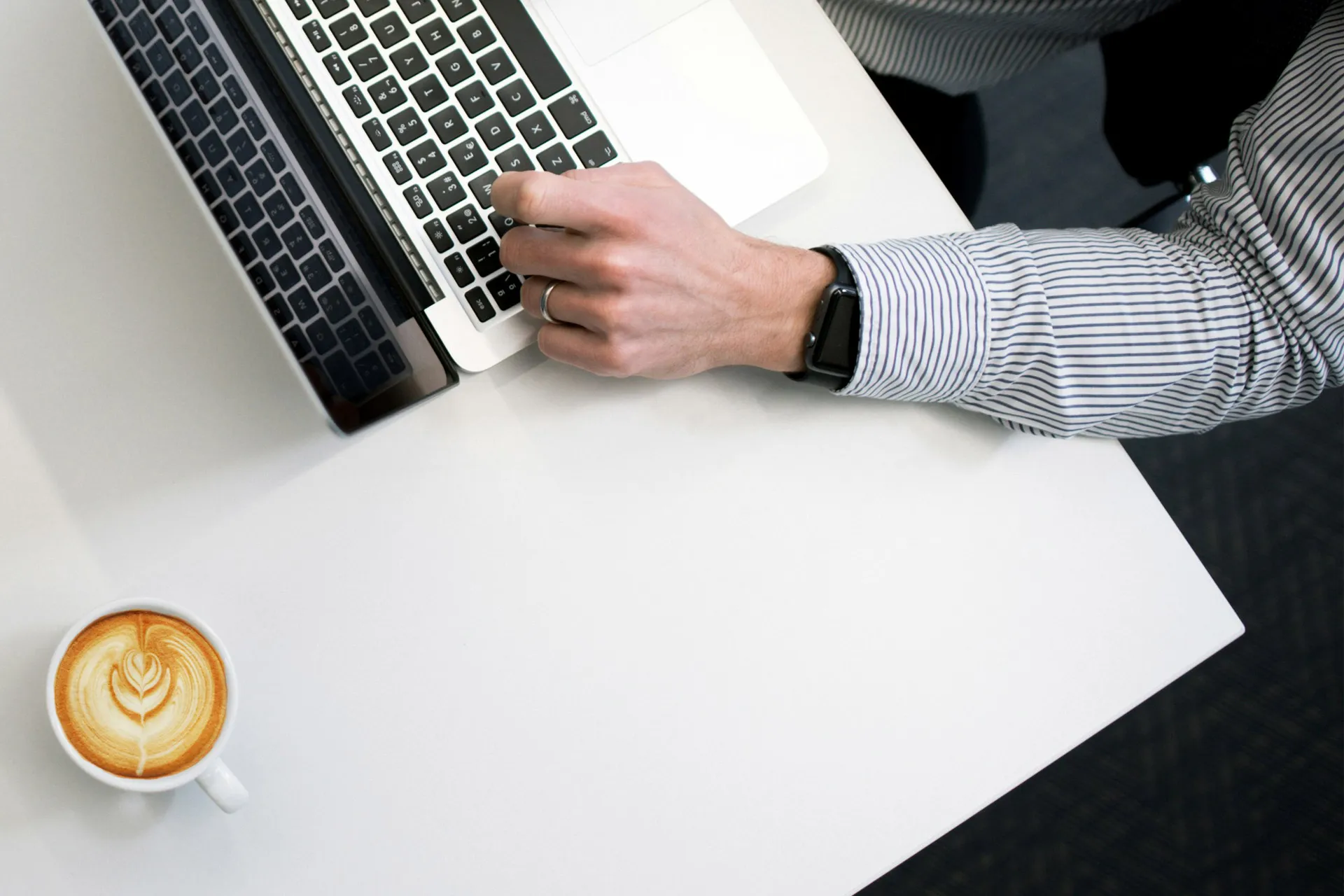 Mann sitter ved PC og rapporterer med en kopp kaffe på bordet