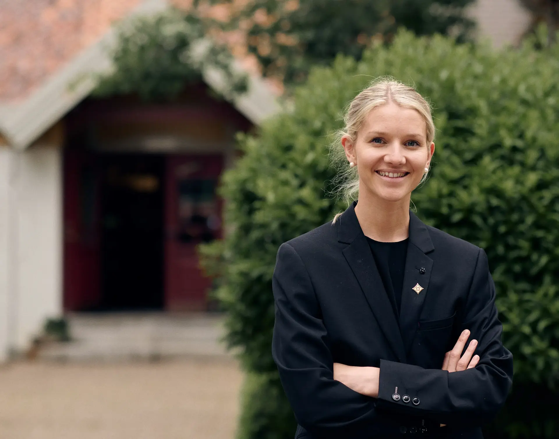 Portrett av dame med en bygning og en hekk i bakgrunnen