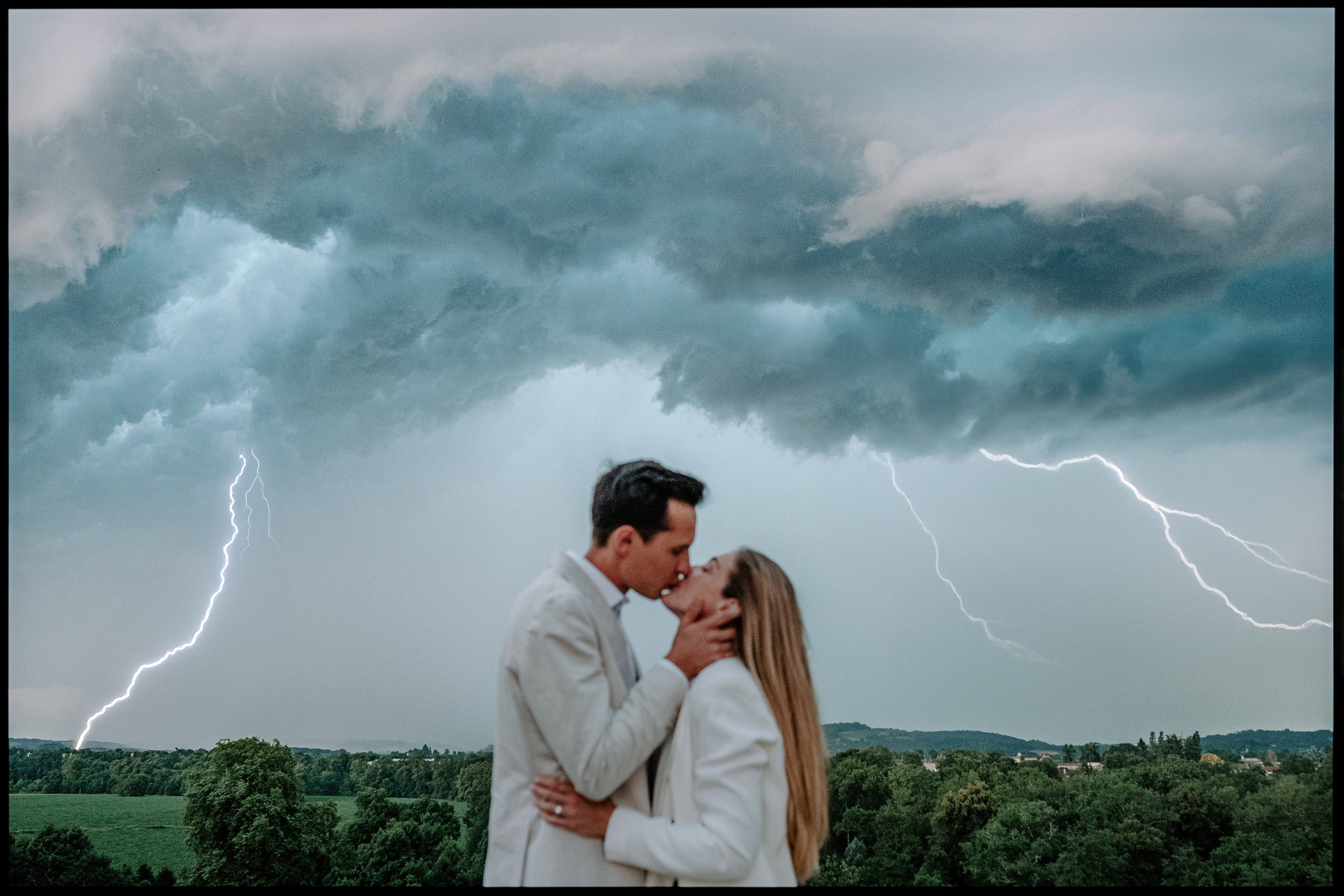 Couple kissing in a field under a stormy sky with lightning
