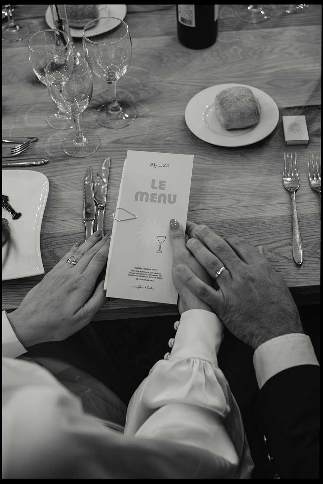 Black and white photo of a couple holding hands over a wedding menu