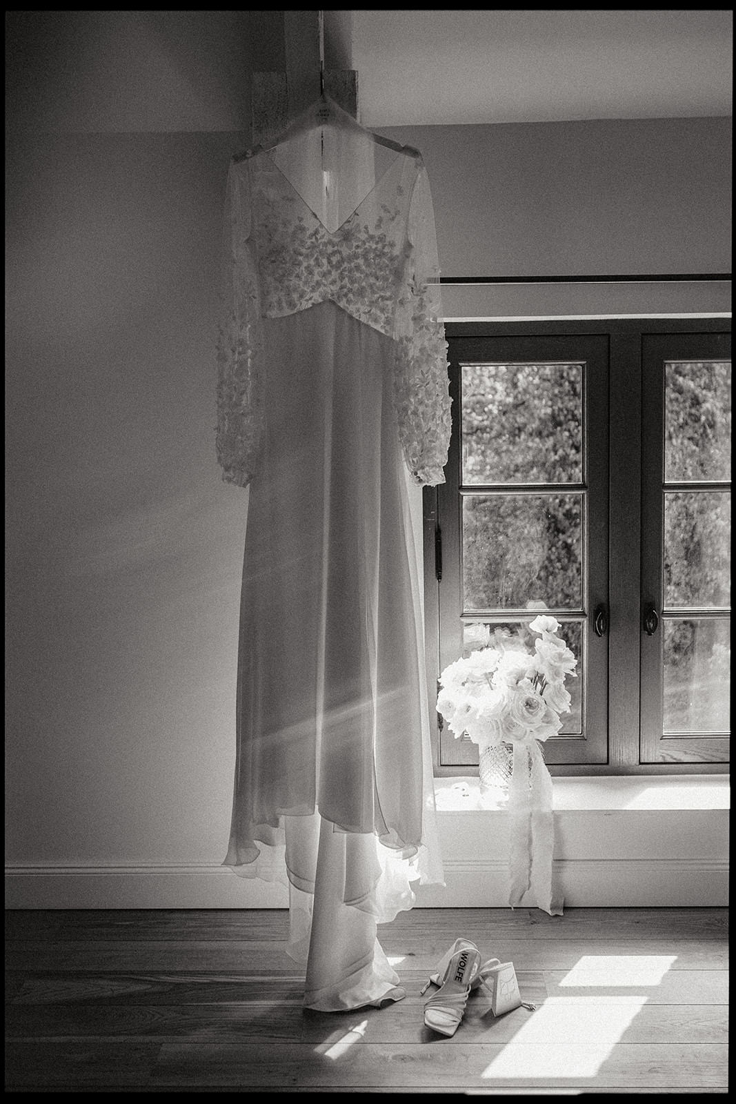 Black and white photo of a wedding dress hanging by a window