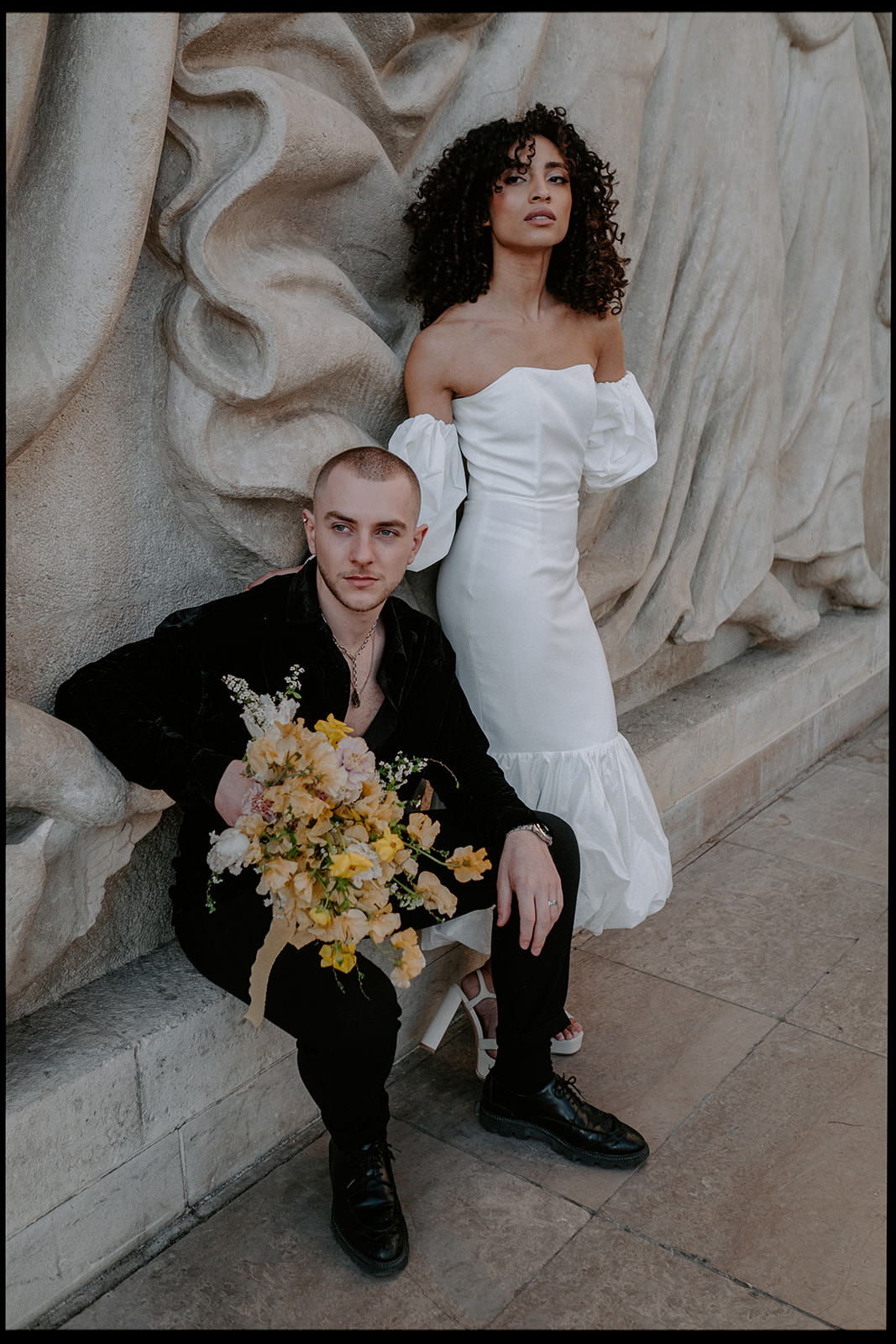 Couple posing on a stone bench with a bouquet of yellow flowers