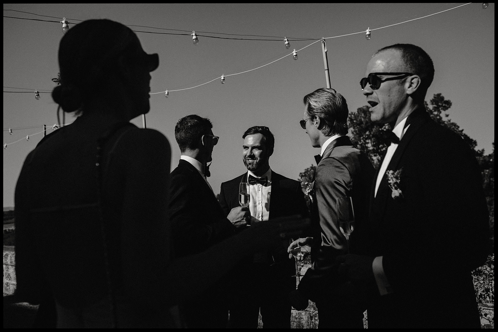 Black and white photo of men in suits chatting at a wedding reception