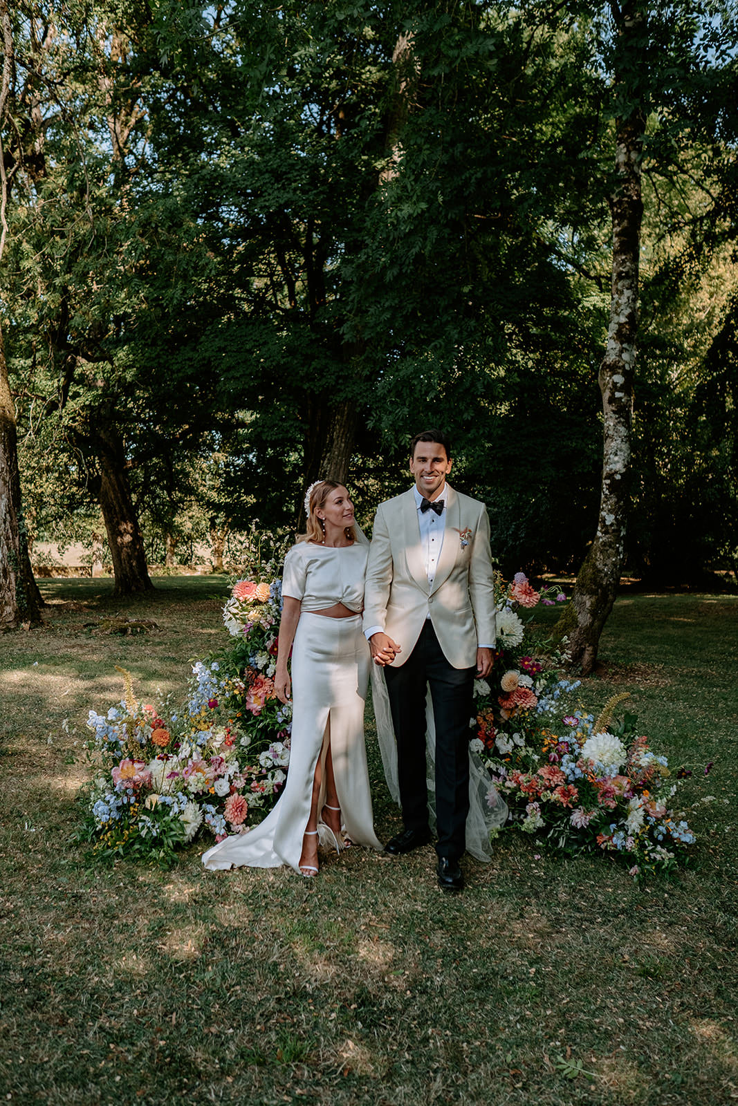 Bride and groom holding hands before a floral arch in a garden ceremony