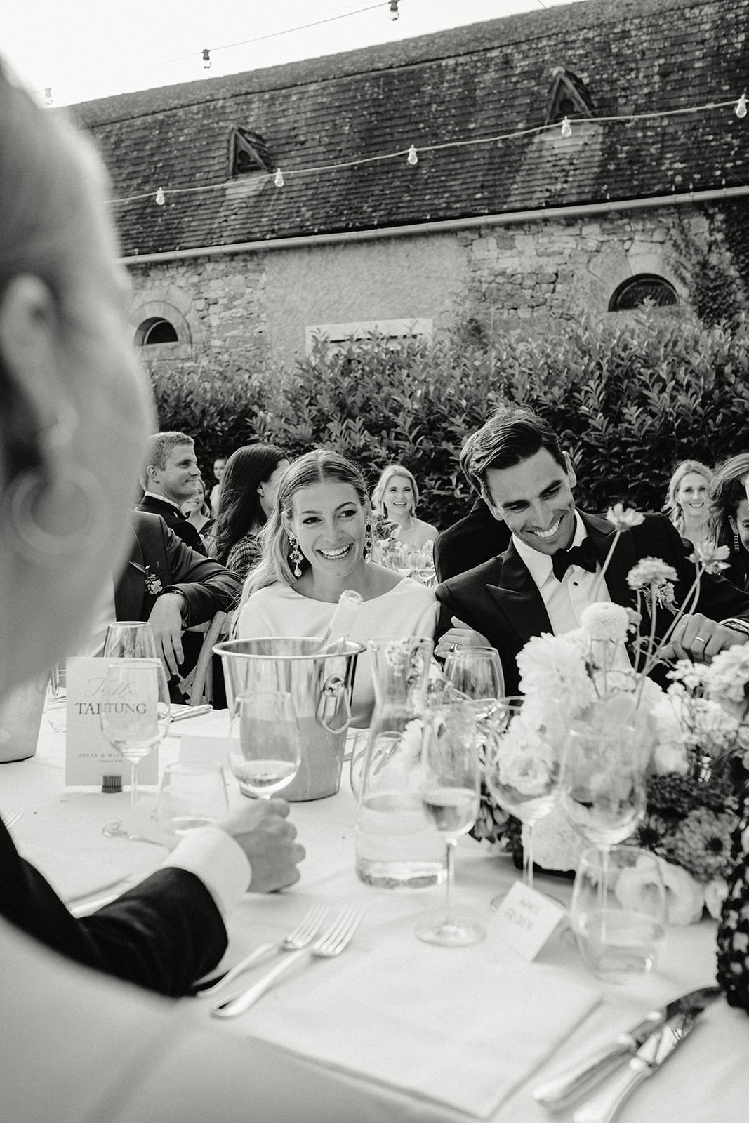 Black and white photo of the bride and groom laughing at the wedding dinner table