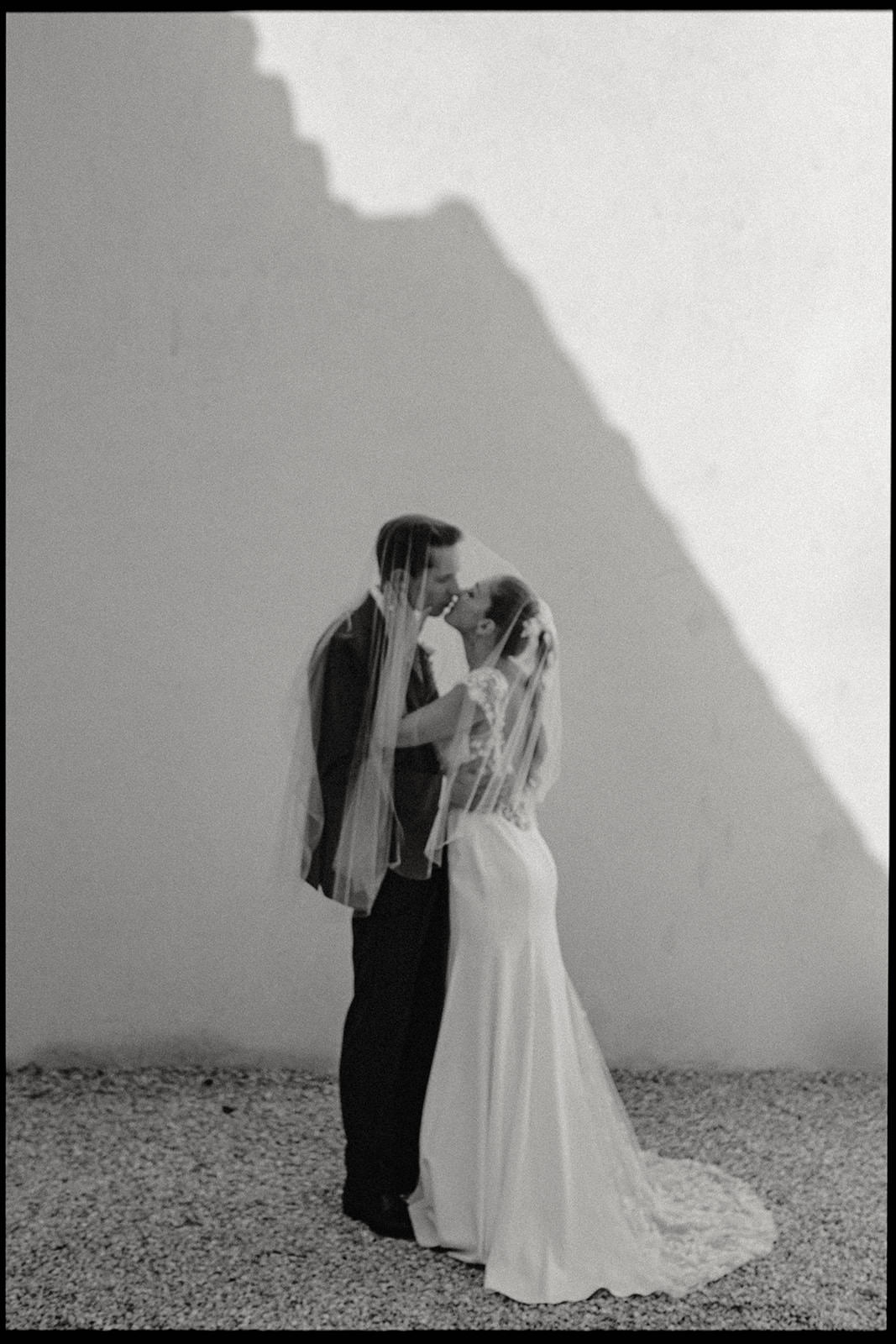 Black and white portrait of a couple kissing against a white wall