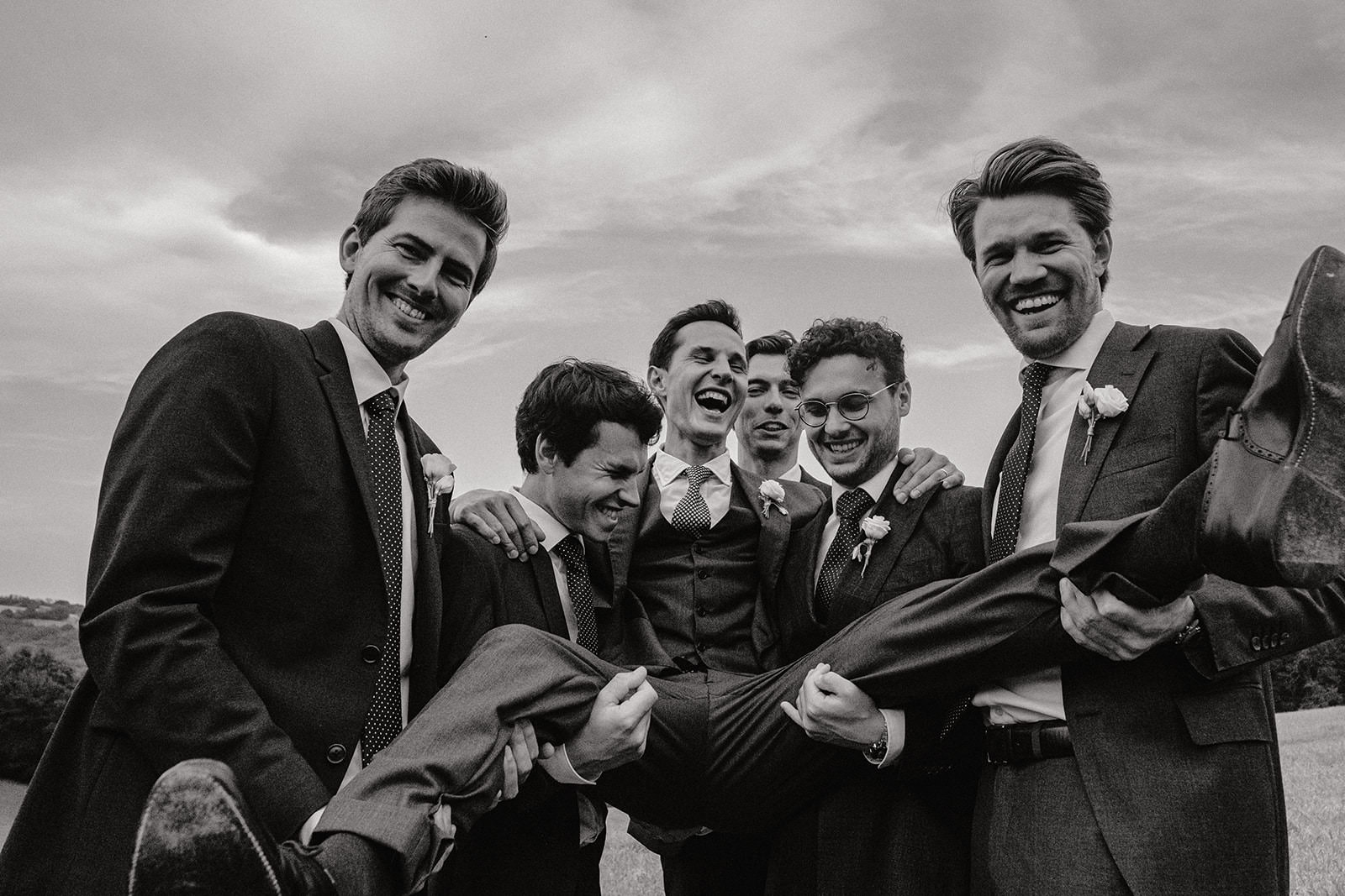 Black and white photo of groomsmen lifting the groom