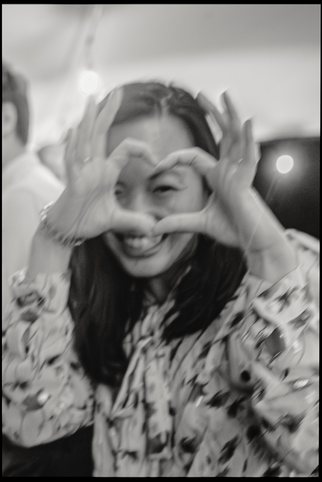 Black and white photo of a smiling wedding guest making a heart with her hands