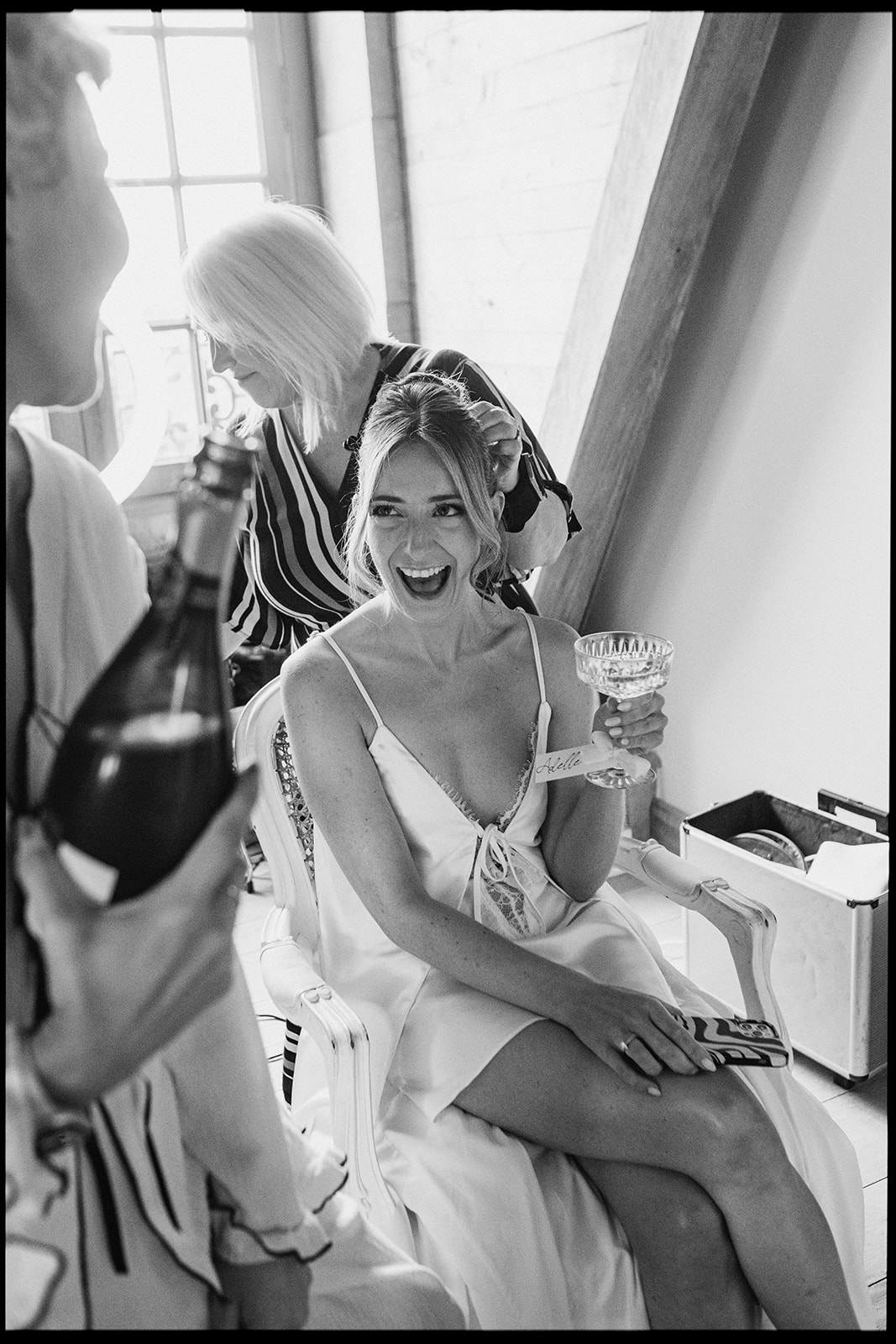 Black and white photo of a bride laughing while getting ready with champagne