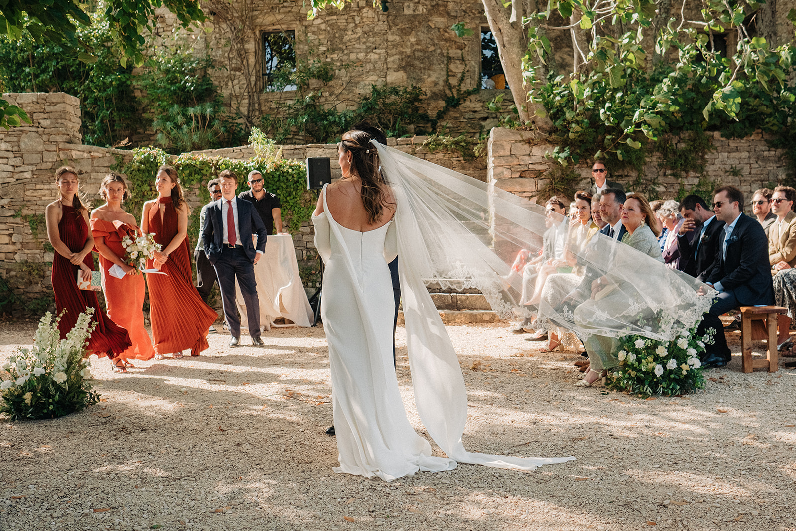 Bride with a long veil walking toward her guests at an outdoor wedding ceremony