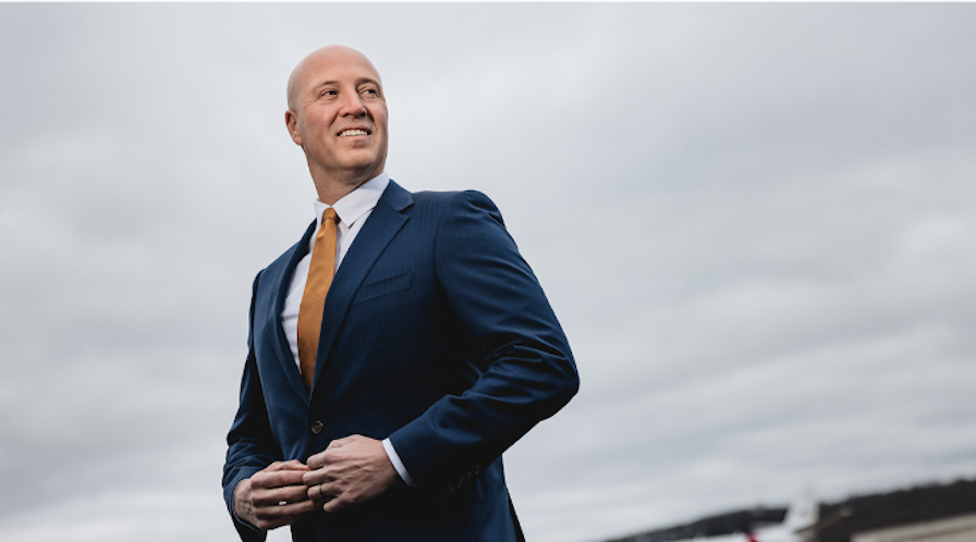 Mike Mikolay CEO of Mikolay Jet Group in business suit, standing in front of an aircraft looking off camera