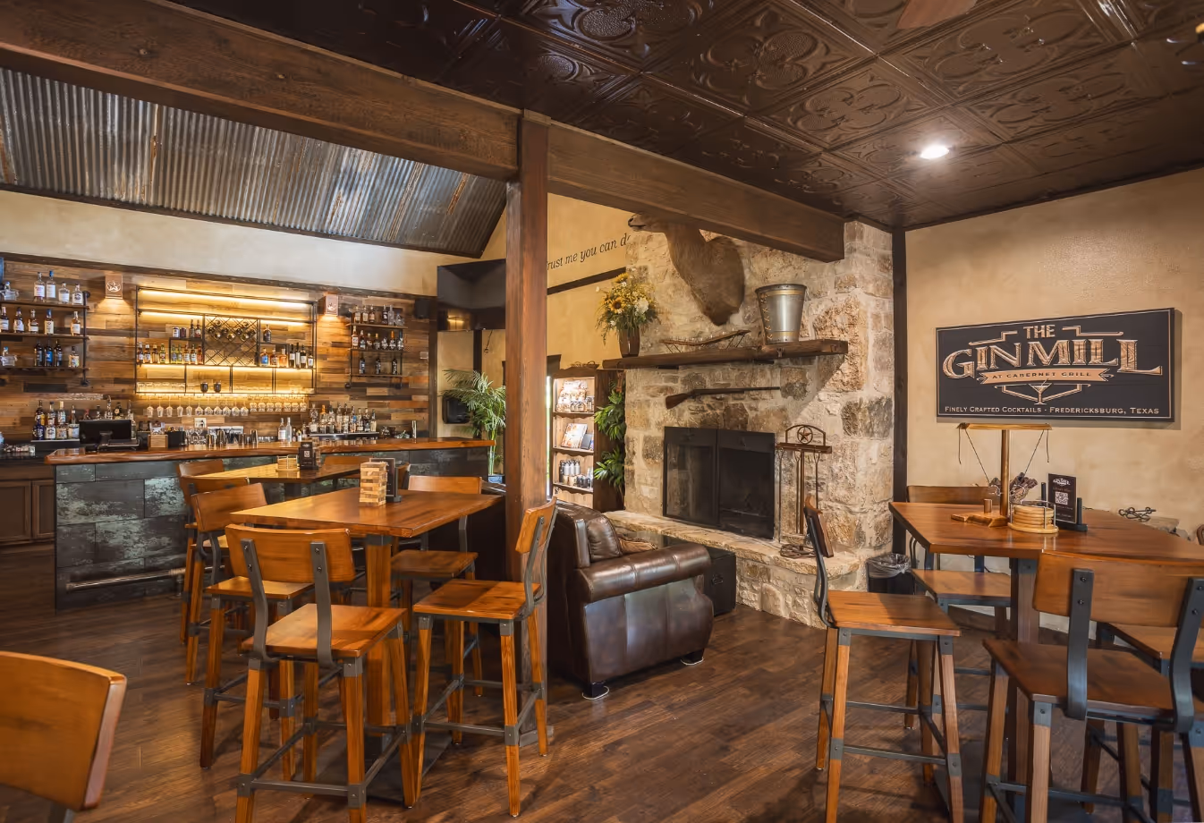 Cozy rustic bar with wooden tables, stone fireplace, and well-stocked bar