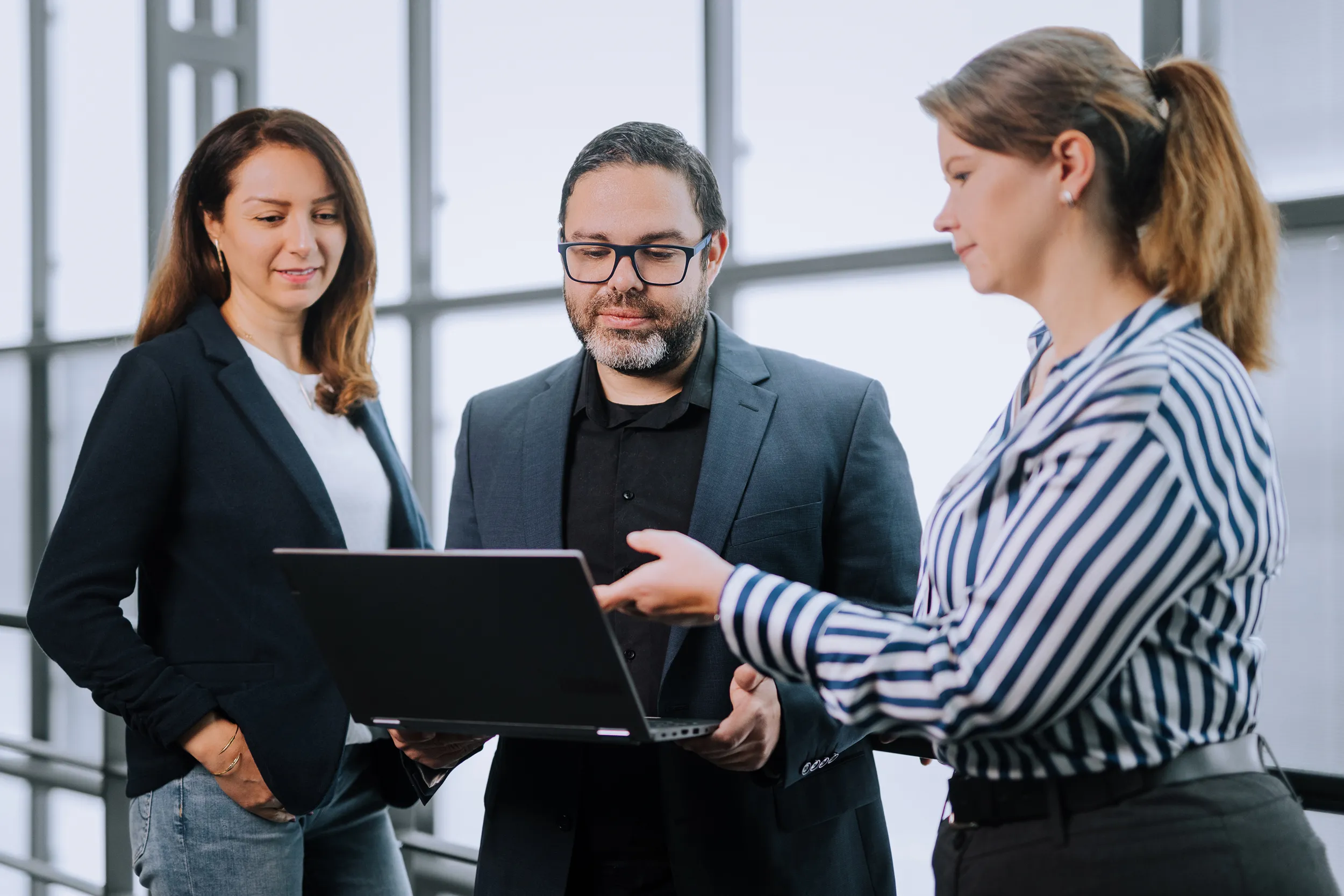 Professionelle Businessfotos München: Drei Kolleginnen und Kollegen besprechen sich am Laptop