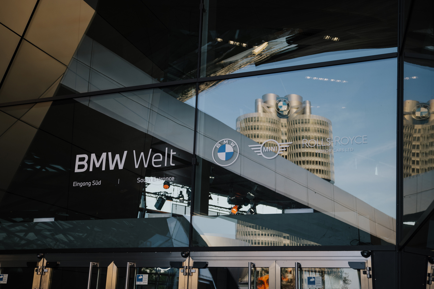 Moderne Architektur der BMW Welt und das berühmte Hauptgebäude in München spiegeln sich in einer Glasfassade – kreative Businessfotografie.