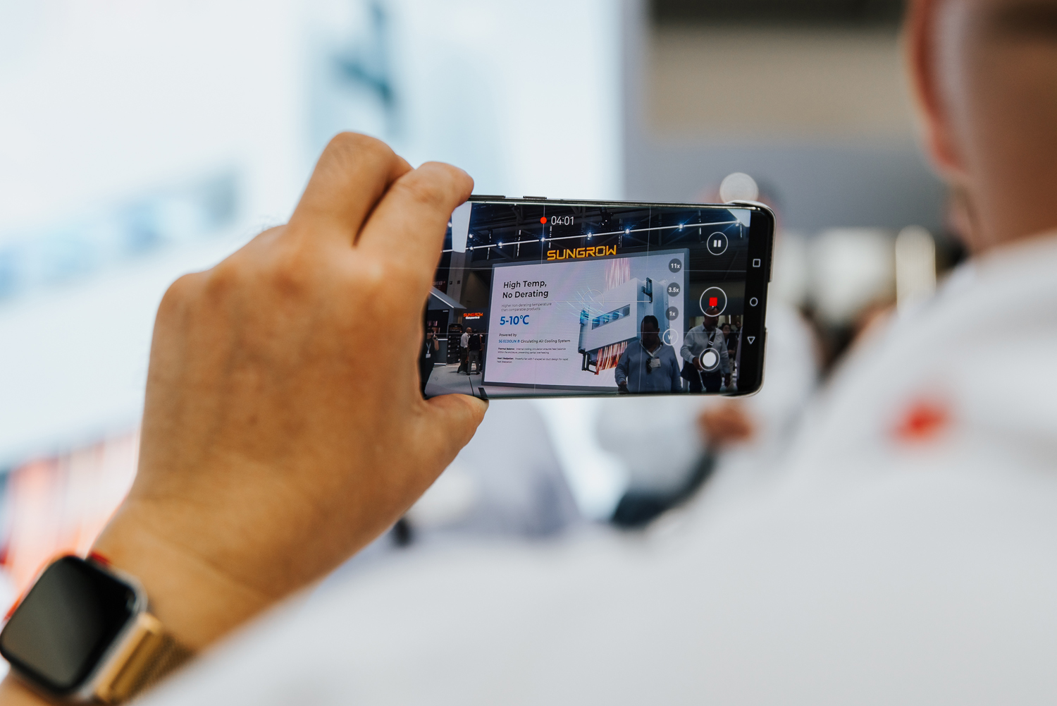 Eventfotograf München: Nahaufnahme eines Besuchers, der ein Display mit seinem Smartphone auf einer Messe fotografiert.