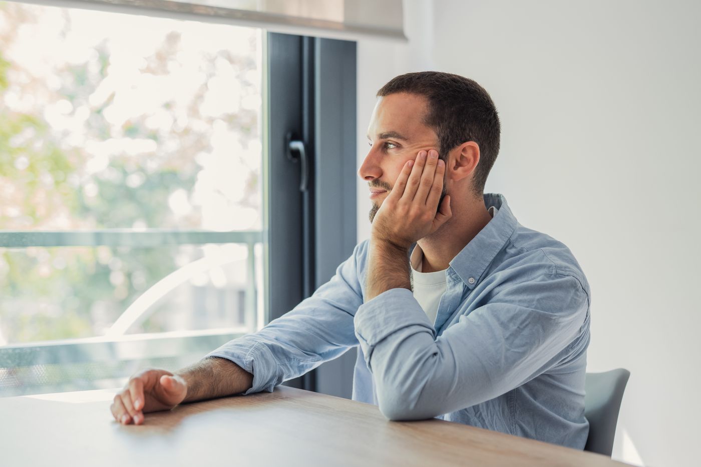 Man sitting at a table by a window, deep in thought