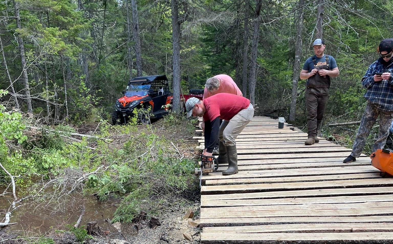 Aroostook County ATV Club building a bridge on maine atv trails. volunteers are building a wooden structure to protect the stream below.