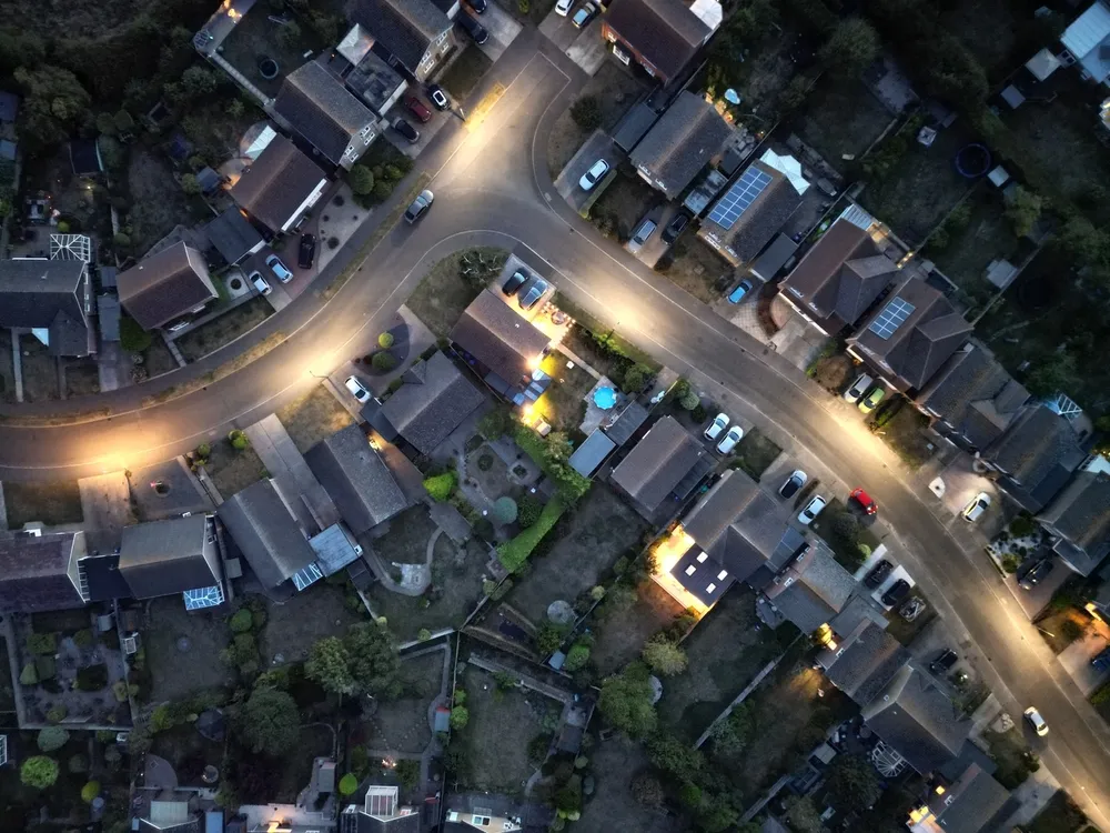 Aerial top-down view of a neighborhood at night. Streetlights can be seen illuminated the curve of the road.