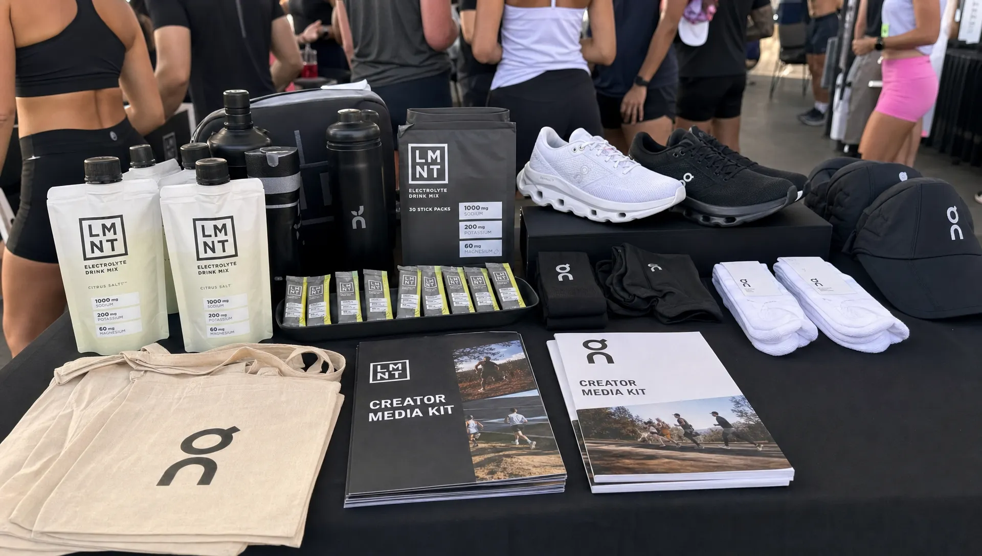 A table at a community fitness event holds product samples, branded packaging, running shoes, training gear, and creator media kits.