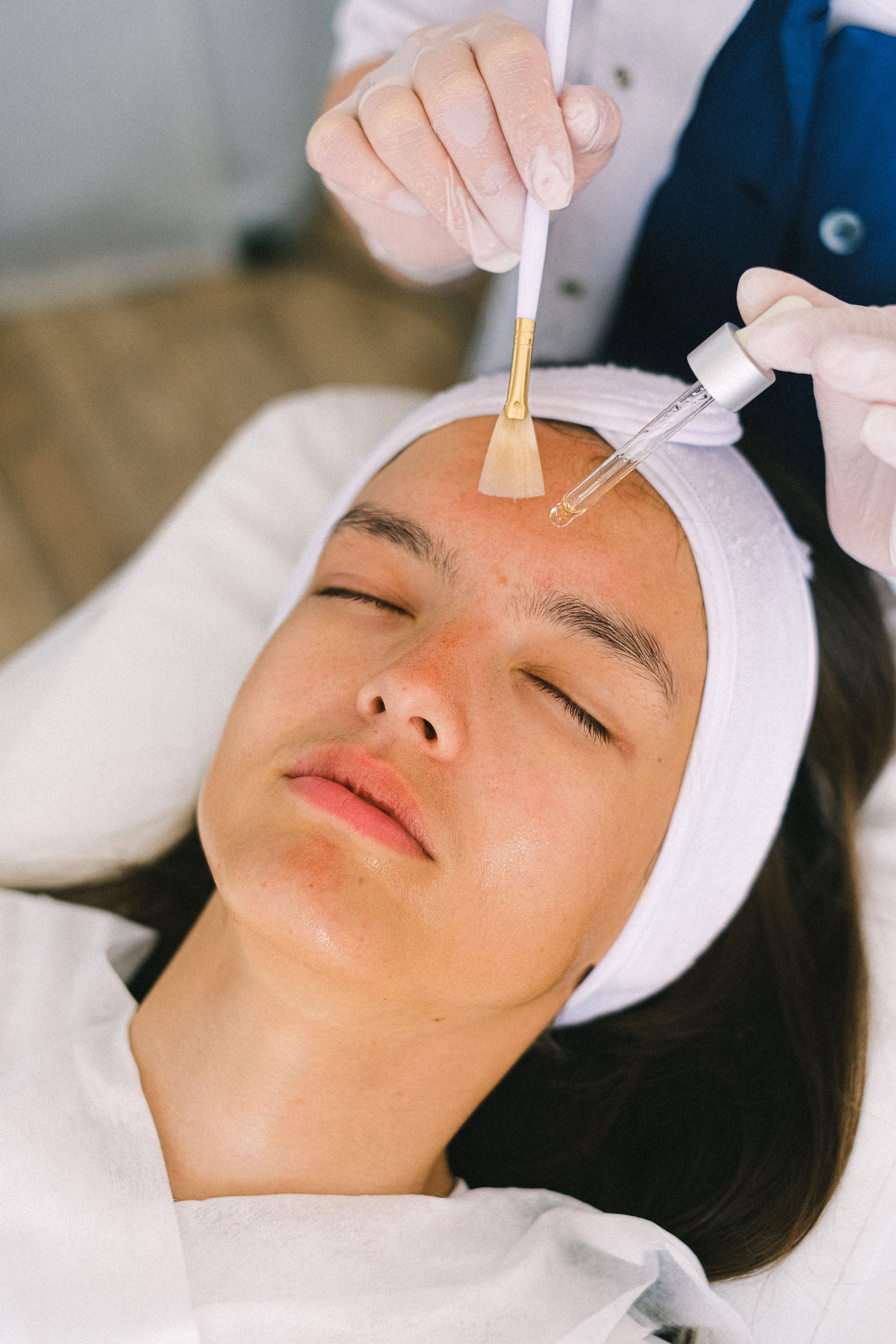 Fan brush and dropper applying a DEJ BioStim peel solution to a client's forehead