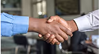 Two people wearing business shirts shaking hands in an office setting.