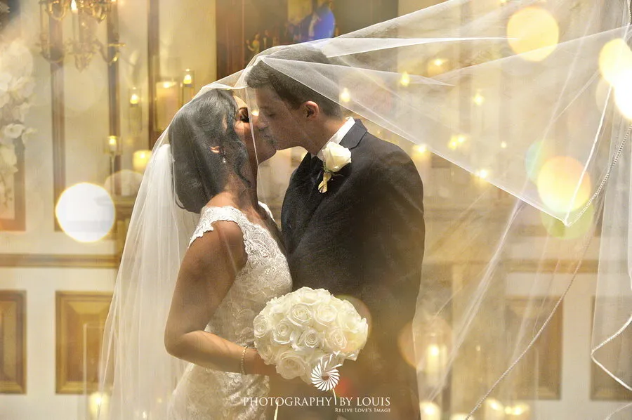 Bride and groom kissing beneath a vail