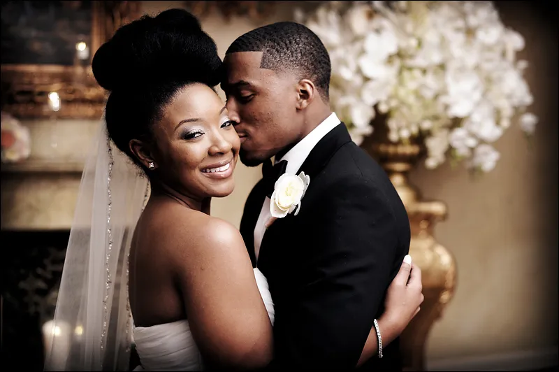 Smiling bride and groom embracing, with the groom gently kissing the bride's cheek during their wedding.